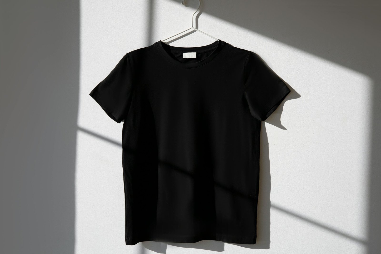 Camiseta Digital Art 3 Minimalist image of a black t-shirt on a hanger with dramatic shadows on a white wall.
